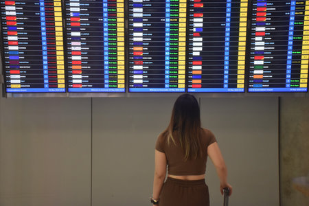 Asian woman carrying travel bag and look at airline schedule board in airportの写真素材