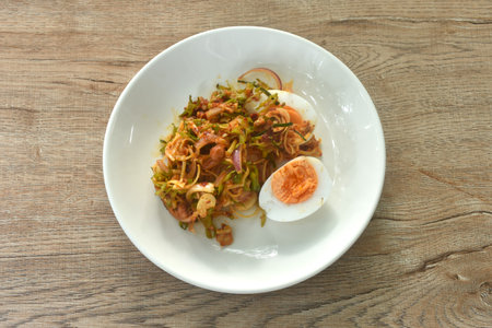 spicy and sour slice wing bean and banana blossom with chop pork sauce topping boiled egg Thai salad on plateの写真素材