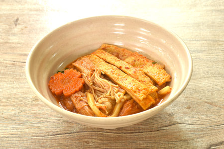 udon noodles topping slice fish tofu and needle mushroom with carot in kimchi soup on bowlの写真素材