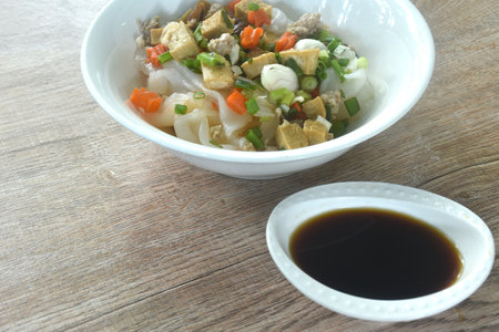 steamed large rice noodles topping chop pork and dice tofu with carrot dressing black soy sauce on plateの写真素材