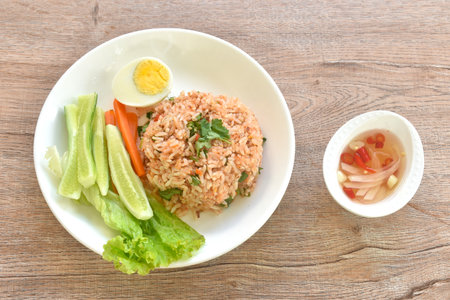 spicy fried rice with mashed salmon topping half boiled egg eat couple fresh vegetable on plate dressing slice chili and garlic fish sauceの写真素材