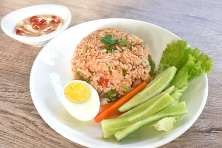 spicy fried rice with mashed salmon topping half boiled egg eat couple fresh vegetable on plate dressing slice chili and garlic fish sauceの写真素材