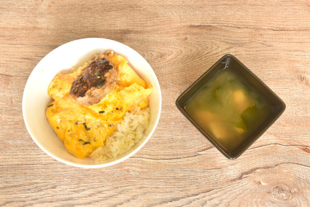grilled hamburg pork steak and creamy egg omelets topping on rice in bowl with miso or soy sauce soupの写真素材