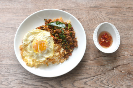 spicy fried chop meat in herb curry topping on plain rice with egg on plate dressing chili fish sauceの写真素材