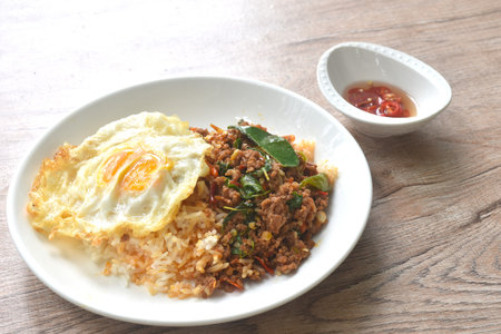 spicy fried chop meat in herb curry topping on plain rice with egg on plate dressing chili fish sauceの写真素材