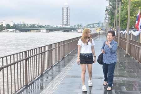 Asian elder woman and daughter enjoy talking with landscape view of Cho phraya river in Thailand on rainy dayの写真素材