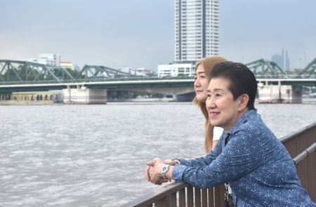 Asian elder woman and daughter enjoy looking landscape view of Cho phraya river in Thailand on rainy dayの写真素材