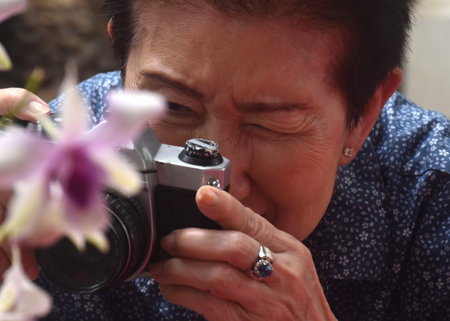 Asian elder woman used film camera shoot pink flower in parkの写真素材