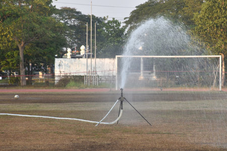 sprinkler splashing water to watering football or soccer grass field in summerの写真素材