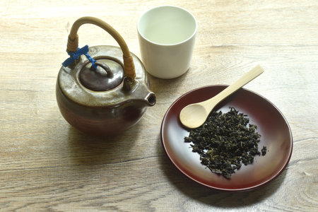 dry tea leaves and wooden spoon with pottery pot and glass on tableの写真素材