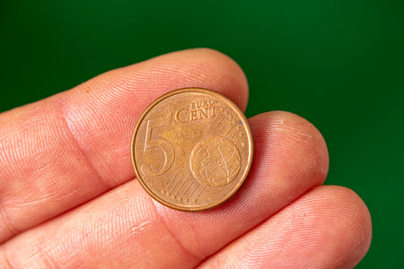 coin face of 5 euro cents in the fingers of the hand. green background.