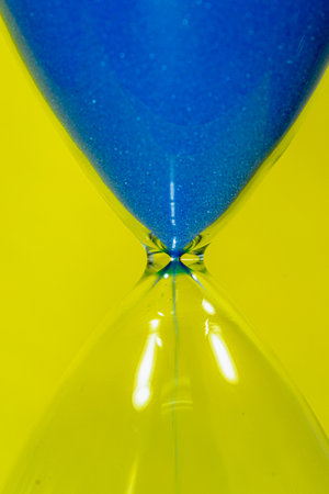 Close up of a blue hourglass on yellow background. Time concept