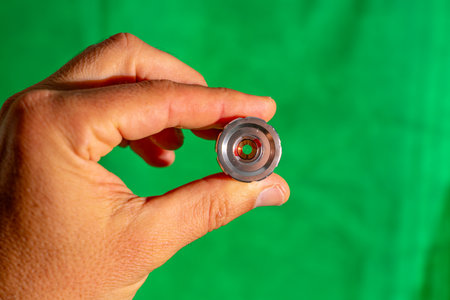 Male hand holding a car oil filter on a green background close up