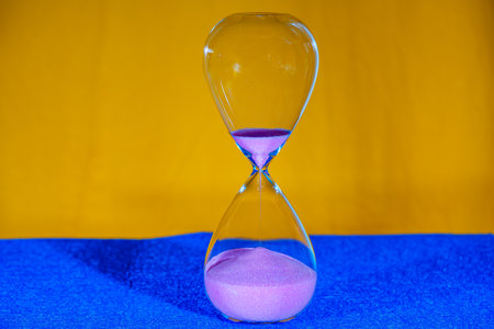 Hourglass on blue and yellow background. Sand running through the glass.の写真素材