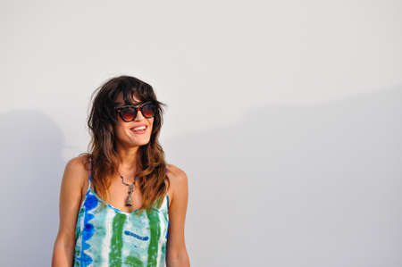 Portrait of young woman smiling with sunglasses and a colorful dress on white background