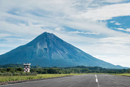 Airport runway in the middle of green nature and next to a volcano in a sunny dayの写真素材