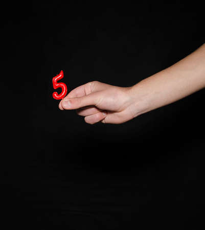 Hand holding up the number against a black background conceptual of numbers, measurement, amount, quantity, accounting, birthday and mathematicsの写真素材