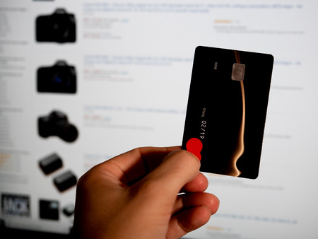 Hand holding a credit card in front of a screen. Shopping online. First person point of viewの写真素材