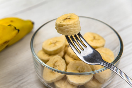 Raw yellow banana fruit slices in a bowl  whit a fork on white wood tableの写真素材