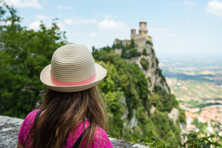 A beautiful touristic girl in the San Marino, admiring the castle on the mountainの写真素材