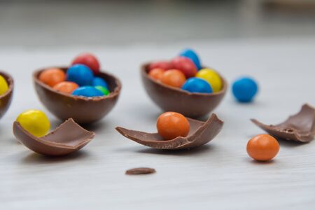 Chocolate Easter eggs and chocolate eggs filled with sweet and colorful candies, on white wood table. Close up.の写真素材
