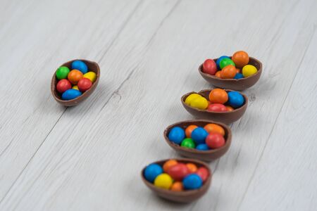 Chocolate Easter eggs and chocolate eggs filled with sweet and colorful candies, on white wood table. Top view.の写真素材