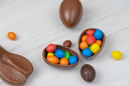 Chocolate Easter eggs and chocolate eggs filled with sweet and colorful candies, on white wood table. Top view, close-up.の写真素材