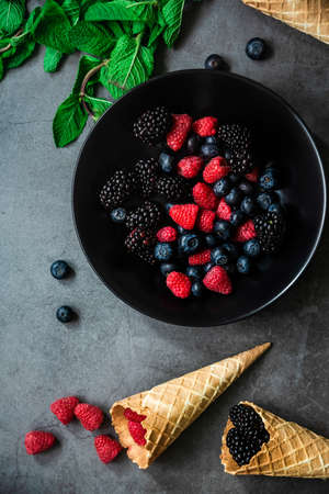 Organic berries served in a black plate on dark metal background, top view. Concept healthy food.