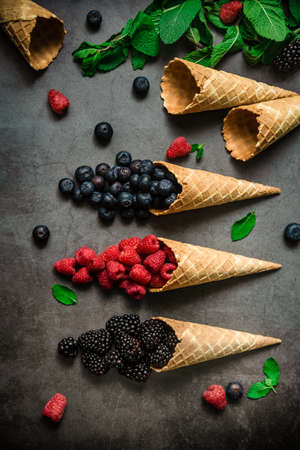 Fresh berries in waffle cones on dark stone background, top view. Concept healthy food and dessert.の写真素材