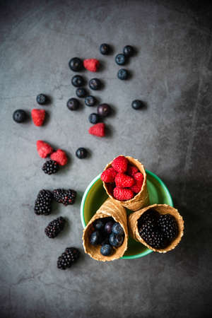 Fresh berries in waffle cones on dark stone background. Top view. Concept healthy food and dessert.の写真素材