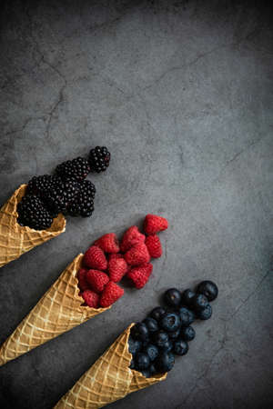 Fresh berries in waffle cones on dark stone background, top view. Concept healthy food and dessert. Copy space.の写真素材