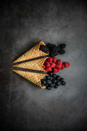 Fresh berries in waffle cones on dark stone background, top view. Concept healthy food and dessert.の写真素材