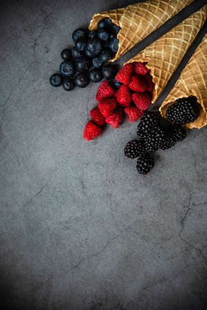 Fresh berries in waffle cones on dark stone background, top view. Concept healthy food and dessert. Copy space.の写真素材