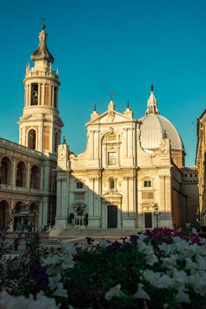 Square of Loreto with background the basilica in sunny day, portico to the side, people in the...