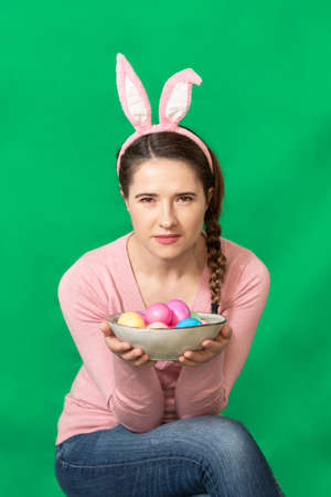 Happy young woman wearing bunny ears holding colored Easter eggs, shooting in a studio.