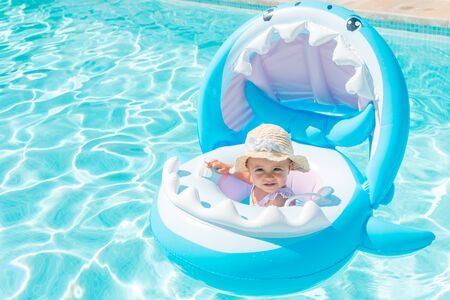 Caucasian girl with hat on a shark-shaped float in the pool