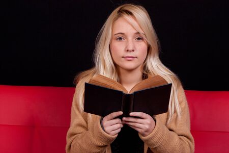 beautiful blond girl reading a book with a dark backgroundの写真素材