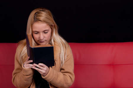 beautiful blond girl reading a book with a dark backgroundの写真素材