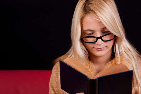 beautiful blond girl reading a book with a dark backgroundの写真素材