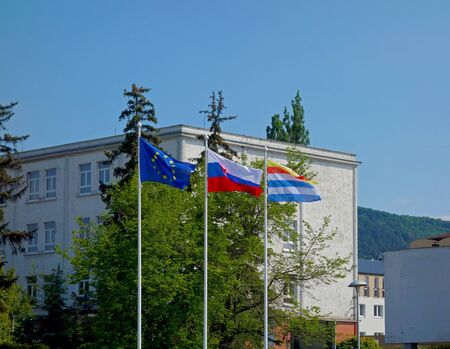 Three flags on poles and in the background a white building