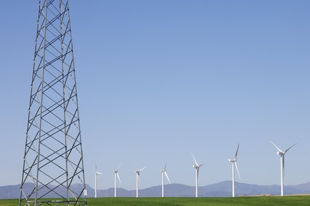 windmills aligned and high voltage electrical line with a clear blue sky