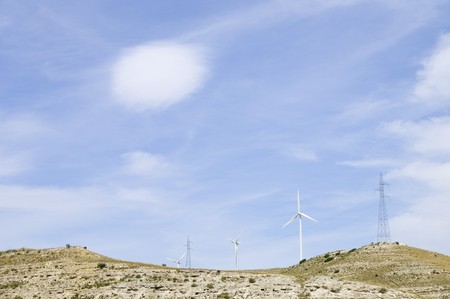 windmills for electric power production and high-tension towers on a hill