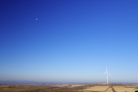 modern windmill for electricity production and moon in the cloudless skyの写真素材