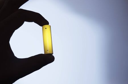 Yellow AA  battery supported by a  hand