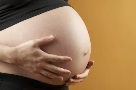 pregnant woman caressing  her belly with orange backgroundの写真素材