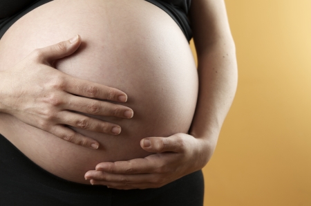 pregnant woman caressing  her belly with orange backgroundの写真素材