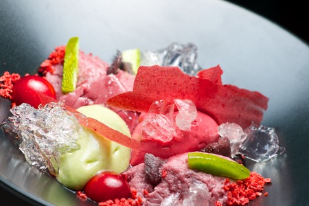 Strawberry and pistachio ice cream with cherries in a black bowl.の写真素材
