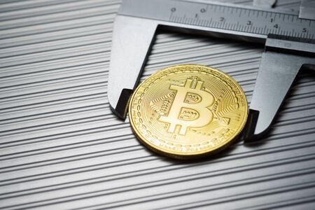 Bitcoin and caliper on a metal table.