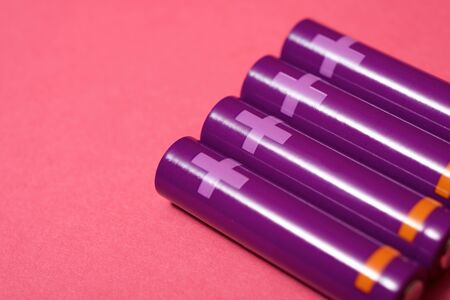 Four small batteries on a pink table.の写真素材