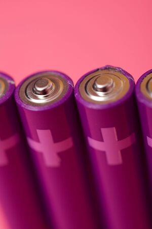 Four small batteries on a pink table.の写真素材